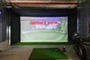 An indoor golf simulator setup with a large projection screen showing a golf course and the text 'CUSTOMIZE WIDTH' with a red arrow, a green turf hitting mat in the foreground, and a golf bag with clubs on the right.
