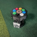 A black 3D-printed revolver-themed toy or prop stand with colorful numbered buttons around a central circular emblem, shown on a green turf-like surface. A small clear bag with black rings hangs from the front.