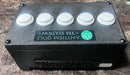 A black control box with five white circular buttons on top and a green 'Anthem Golf - Tee Station' logo sticker on the front, placed on a speckled granite countertop.