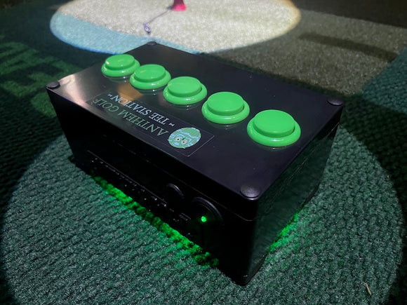 A black electronic golf tee system box with five green push buttons on top and green LED lighting on the bottom, placed on a textured green carpet.
