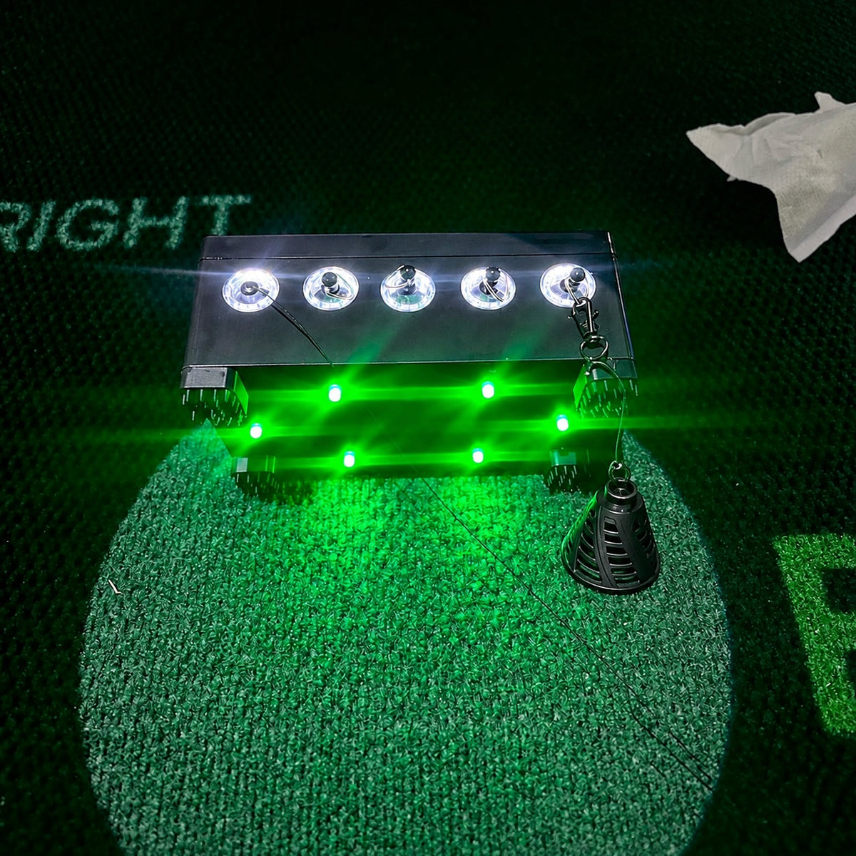 Lighted Anthem Golf Tee Station Birtee Edition from a low angle, green floor lighting on, black size 8 Birtee on the last tether