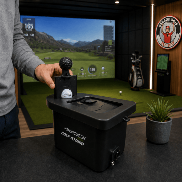 A hand placing a golf ball into a black ball washer inside a Garage Golf simulator studio, with the simulator screen, golf clubs, and the Garage Golf wall logo in the background.