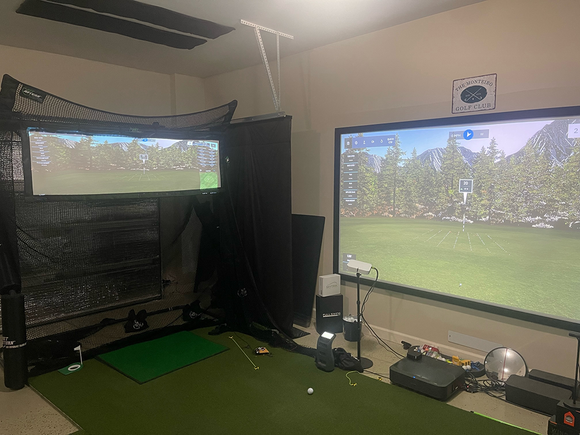 Home golf simulator setup with The Net Return Split Screen Accessory (net not included); a large simulator screen displays a virtual course, with various golf equipment and cables visible on the floor. Screens are not returnable.