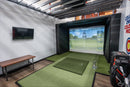 Indoor golf simulator setup with screen displaying a golf course and bench on the side.