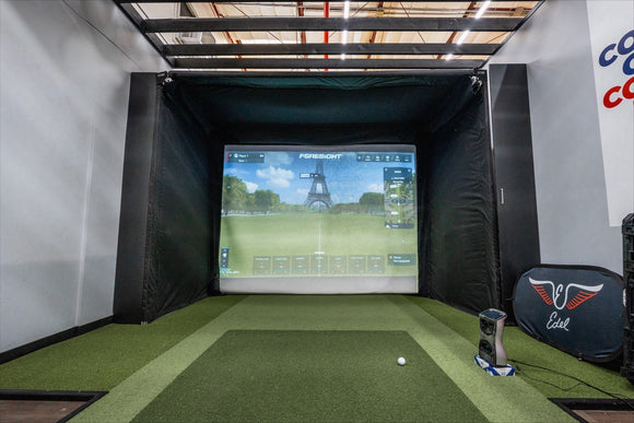 Indoor golf simulator setup with screen displaying a golf course and club equipment on a green floor.