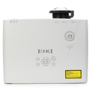 An EIKI brand white home theater projector with a black lens cover, featuring a central control pad, lens shift dial, and a yellow warning label on the front, set against a plain white background.