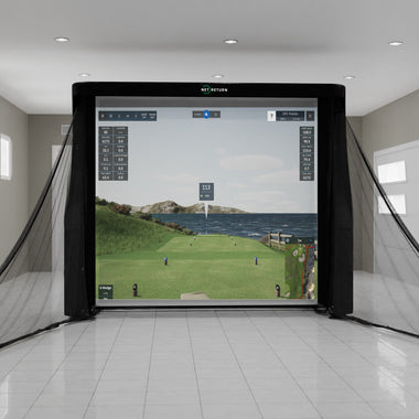 Indoor golf simulator setup with a digital screen displaying a golf course scene, surrounded by protective netting in a bright room.