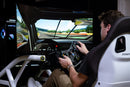 Person using a racing simulator with a detailed dashboard and steering wheel.