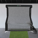 A golf practice net with a grass mat in front and a golf bag with clubs to the side, set in an indoor space.