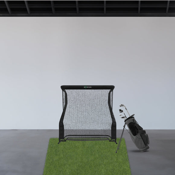 A golf hitting net set up indoors on a patch of artificial grass with a black golf bag and clubs next to it.