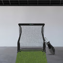 Golf hitting net set up indoors on a patch of artificial grass next to a golf bag.