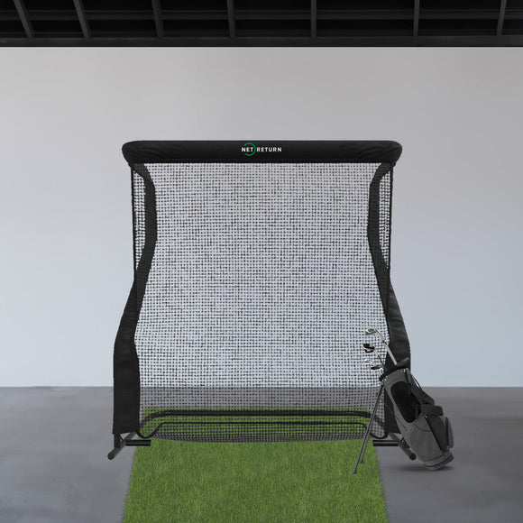 A golf practice net setup with an artificial grass mat and a golf bag stands indoors against a white wall.