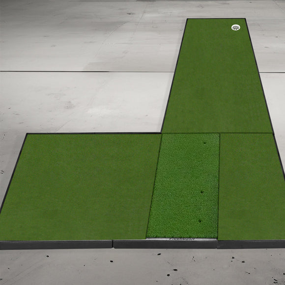 A green golf putting mat on a gray concrete floor, featuring a ball near the hole on a long, L-shaped design.