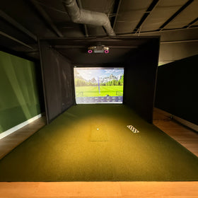 Rain or Shine Golf Studio Turf Sim Flooring Kit inside a golf simulator enclosure, straight on view showing the SwingTurf hitting area set flush into the turf